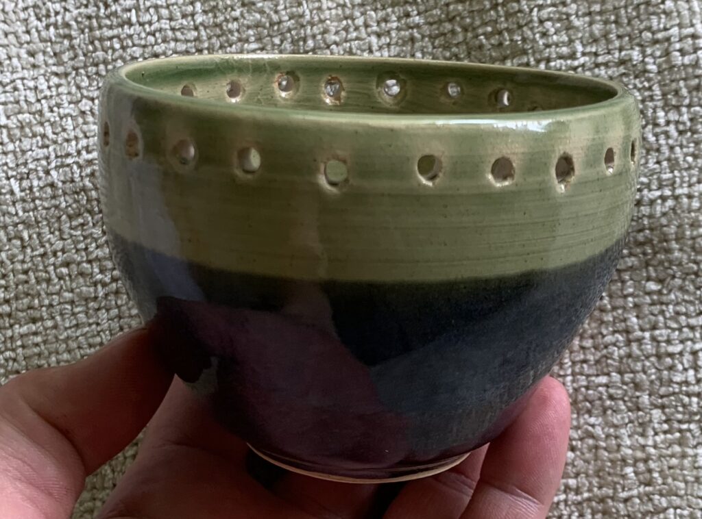 blue and green ceramic bowl with holes around its top edge