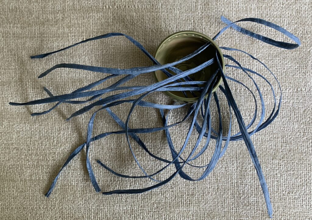 Ceramic bowl with lengths of paper yarn threaded through the holes