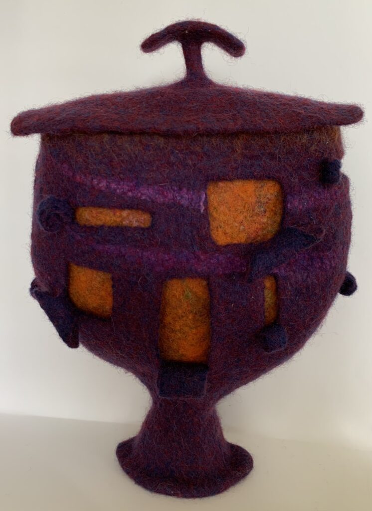 A purple and orange felted vessel with a flared foot and a lid with a handle
